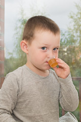 a little boy himself obediently drinks the medicine prescribed by the doctor from a measuring cup. Vertical photo. Looks into the camera.