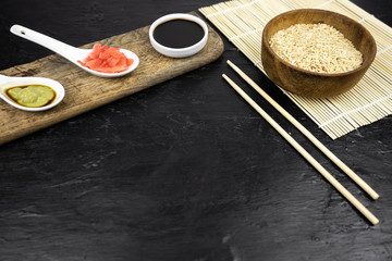Japanese kitchen background with bamboo mat, chopsticks, soy sauce, pickled ginger and brown rice