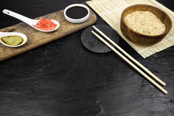 Japanese kitchen background with bamboo mat, chopsticks, soy sauce, pickled ginger and brown rice