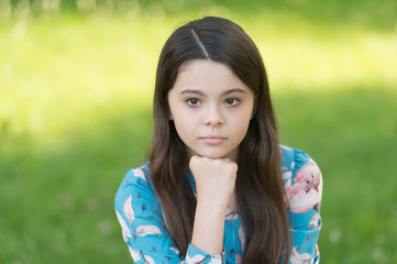 Little girl with long hair relaxing in park sunny day green grass background, sad thoughts concept