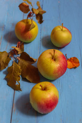 Four apples with leaves are lying on a wooden table