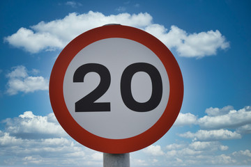 Twenty miles per hour speed limit sign, isolated against blue sky and white clouds background. Taken in UK.