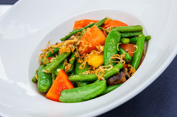 Plate of baked green beans mixed with pea pods and carrot