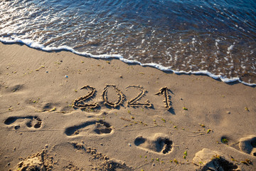 The numbers 2021 are written in the sand. New year on the beach. Sea coast, wave. Natural background. Place for your text. Summer in winter.