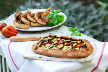 Sausages and vegetarian pies with vegetables and herbs on a wooden table in the garden. Rustic style.