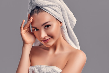 Cute attractive girl with towel on her head isolated on gray background. Skin care concept. Spa treatments, cosmetology, make-up.