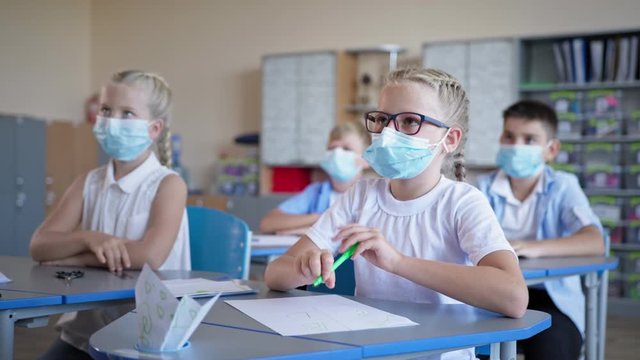 schoolchildren in medical masks raise their hands sitting at a desk, pupils back at school after quarantine and lockdown