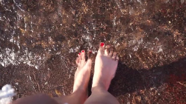 Women's feet splashing in sea water on the beach. Closeup, slow motion