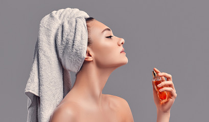 Cute attractive girl with a towel on her head uses perfume isolated on a gray background. Skin care concept. Spa treatments, cosmetology, make-up.