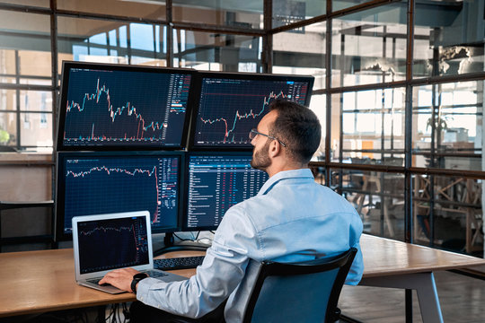 Stock Traiding. Trader sitting at office analyzing price flow on digital screen browsing laptop monitoring market concentrated back view