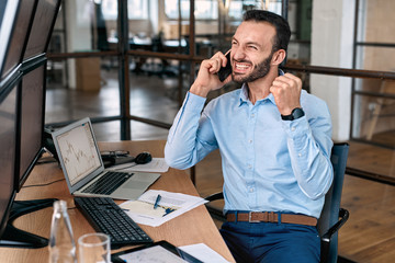 Stock Traiding. Trader sitting at office talking with colleague on smartphone hands in fists...