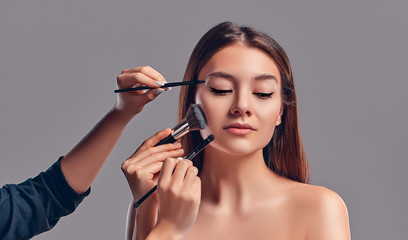 Fototapeta premium Cute attractive girl with makeup brushes isolated on gray background. Beauty salon, make-up.