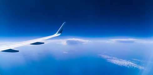 panorama über den wolken mit flugzeug flügel, tief blaue wolkenlandschaft mit blick auf den ozean und weit reichendem horizont   