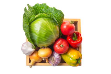 A set of vegetables: cabbage forks, tomatoes, bell peppers, onions and garlic in a wooden box isolated on a white background. Harvest concept. Healthy eating. Top view