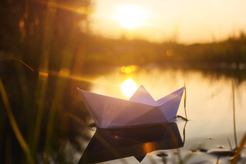 A paper boat floats on the water at dawn. Creative concept of outdoor recreation, river, travel....