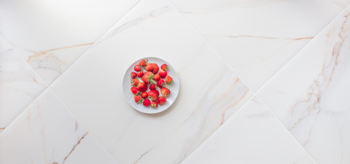  A plate of strawberries on white marble tile with copy space. Red berries on a white kitchen, summer concept