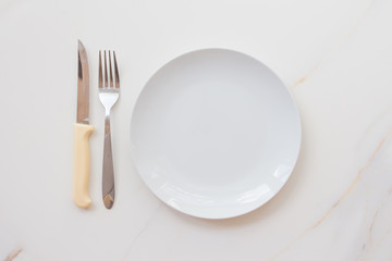  Empty white plate with cutlery on a marble table, saucer, fork and knife. The concept of diet, fasting