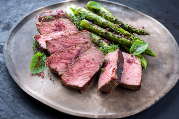 Barbecue dry aged wagyu roast beef steak with green asparagus and lettuce offered as close-up on a...