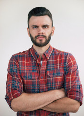 Close up portrait of a handsome serious bearded man in a checkered shirt with crossed arms while he is looking on camera