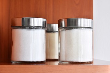 White sugar in glass jar. Three transparent jar with sugar, selective focus. Unhealthy carbohydrates. Food products in domestic kitchen. Backing ingredient. 