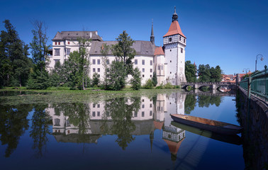 Photograph of Blatna Castle, its reflection in the lake and a small boat.