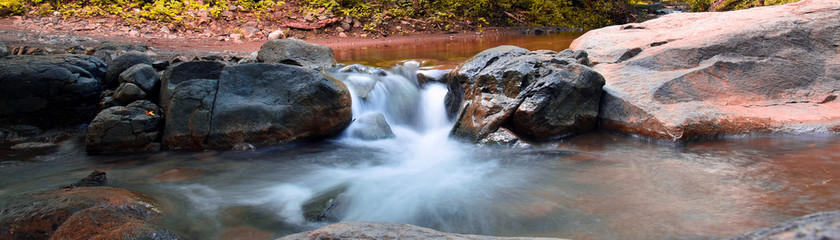 Waterfall panorama view in autumn with rocks and foliage. Panorama view.