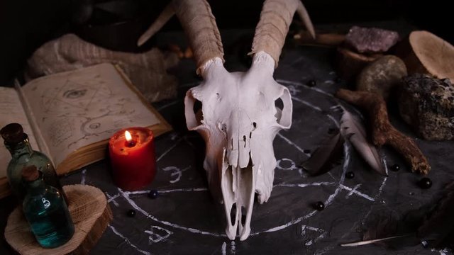 White goat scull with horns, open old book, runes, black candles on witch table. Occult, esoteric, divination and wicca concept. Halloween and Day of the dead concept.