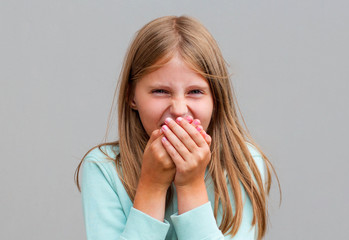 Happy preteen girl covering her mouth and laughing isolated on gray background