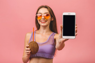 Sexy beautiful young woman wearing swimsuit isolated over pink background. Showing phone screen.