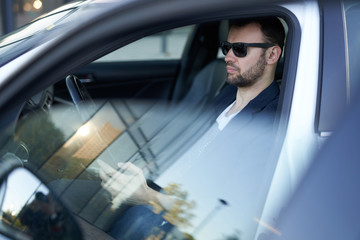 An adult businessman is sitting in his new car and browsing some news