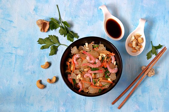 Refreshing salad with pomelo, shrimps, carrots and cashew nuts in a black bowl on a light blue background. Asian cuisine.