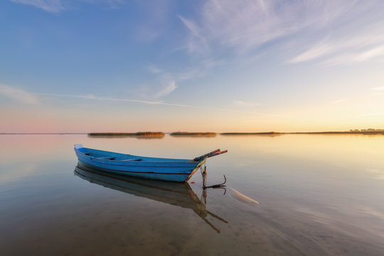 Lonely boat in calm lake. The silhouette is reflecting on the water. Beautiful summer day. Amazing sunrise. Blue sky with clouds. Location place Svityaz lake, Ukraine, Europe.