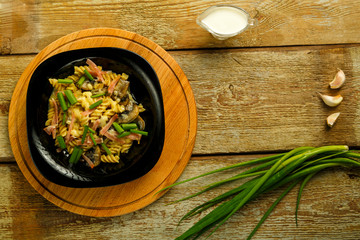 Black plate with pasta with ham and mushrooms in a creamy sauce on the table with a fork near the ingredients.