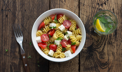 Homemade salad with pasta, tomatoes, feta cheese and spices on wooden table. simple delicious food. top view, space	