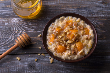 Delicious oatmeal porridge with baked pumpkin, honey and nuts in ceramic bowl on wooden table. healthy homemade breakfast. selective focus
