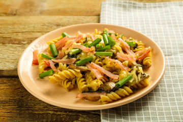 a plate with pasta with ham and mushrooms in a creamy sauce on the table with a fork on a napkin next to the cream.