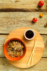 Funchoza with vegetables and mushrooms in a clay plate on a round stand next to chopsticks and soy sauce. Vegetables next to it.