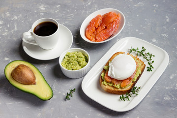  Poached egg with smoked salmon, toasted bread , avocado and coffee on a white plate. Sandwich for breakfast.
