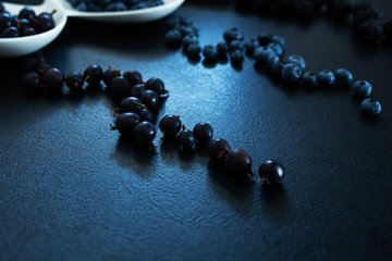 Set of different types of black berries in a white plate on a black table. Stylish seasonal vitamins