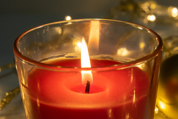Red christmas candle, burning candle fire on a table with holiday garland close up
