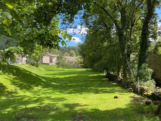 Fototapeta na wymiar Grassy area, with old trees, behind some cottages in the village of Kettlewell, Skipton, UK