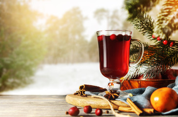 Glass of mulled wine with ingredients on a wooden table against the background of winter forest.