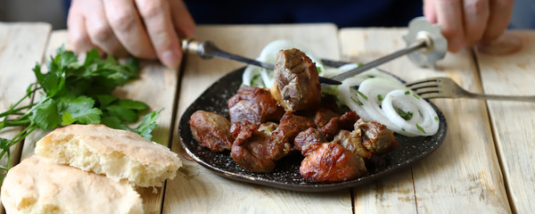 Selective focus. A man with a fork and knife eats a barbecue with onions. A plate with a kebab.
