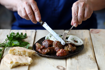 Selective focus. A man with a fork and knife eats a barbecue with onions. A plate with a kebab.