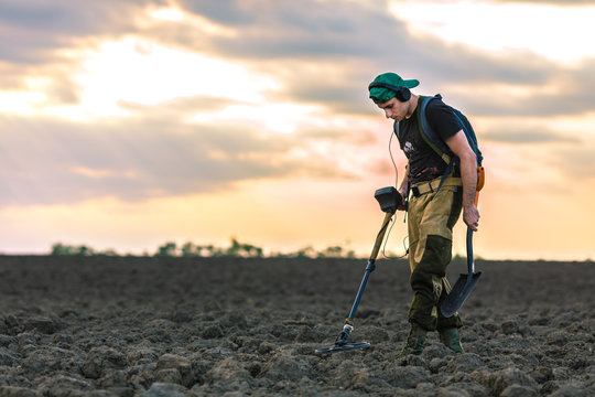 Treasure hunter with metal detector in a field at sunset