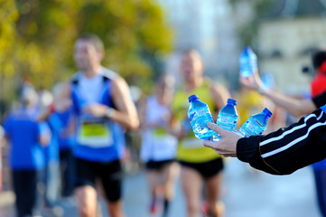 hand with 3 small bottles of water offering water to runners at a marathon refreshment