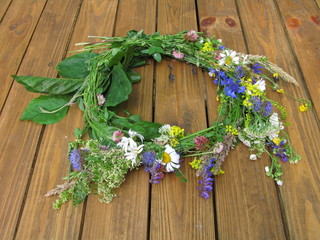Wreath made from meadow flowers on a wooden table - oxeye daisies, pink clover, leaves, eastern Poland