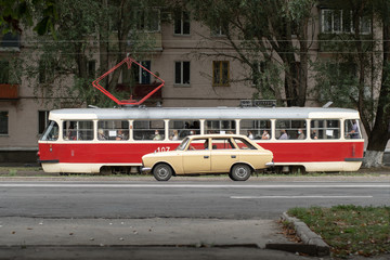 Fototapeta na wymiar Konotop, Sumy Oblast, Ukraine - 24 August, 2020: Old Soviet Tatra tram and car on the road, side view. Transport of the Soviet Union.