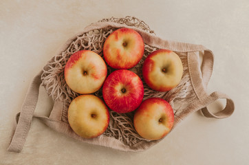 Red apple and string bag on a beige textured background. Ripe apples on the table and copy space. Summer or fall season.