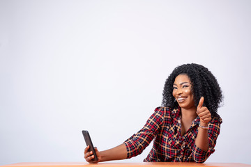 beautiful black lady sitting holding her phone, smiling and giving a thumbs up